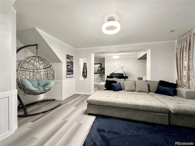 living area with crown molding, a textured ceiling, visible vents, a wainscoted wall, and wood finished floors