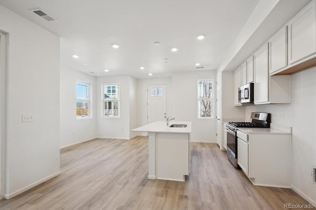 kitchen with sink, light hardwood / wood-style flooring, appliances with stainless steel finishes, an island with sink, and white cabinets