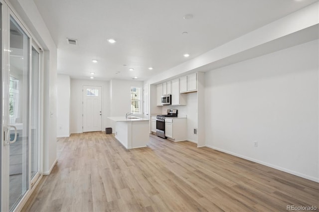 kitchen featuring sink, appliances with stainless steel finishes, an island with sink, light hardwood / wood-style floors, and white cabinets
