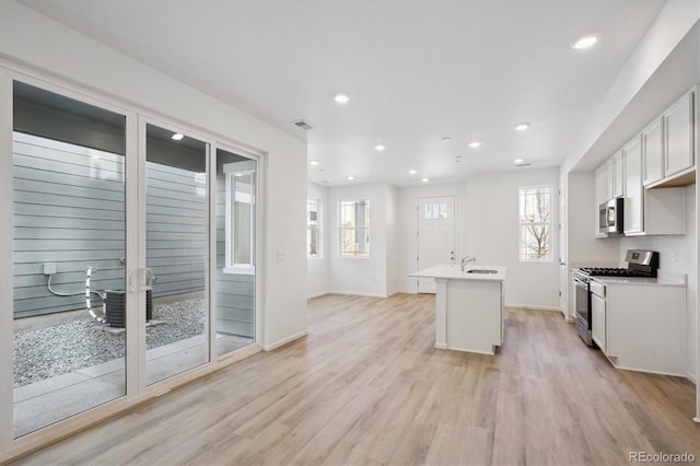 kitchen featuring a center island with sink, light wood-type flooring, plenty of natural light, stainless steel appliances, and white cabinets