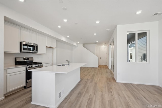 kitchen featuring appliances with stainless steel finishes, an island with sink, sink, white cabinets, and light hardwood / wood-style floors