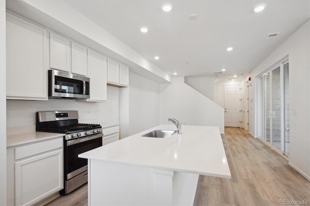 kitchen featuring appliances with stainless steel finishes, sink, white cabinets, light hardwood / wood-style floors, and a center island with sink