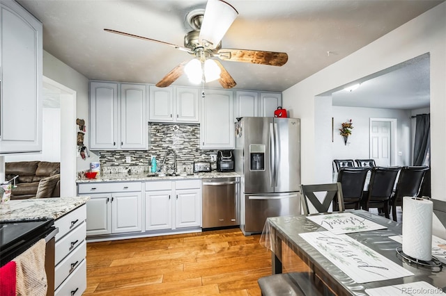 kitchen featuring sink, stainless steel appliances, tasteful backsplash, light stone countertops, and light wood-type flooring