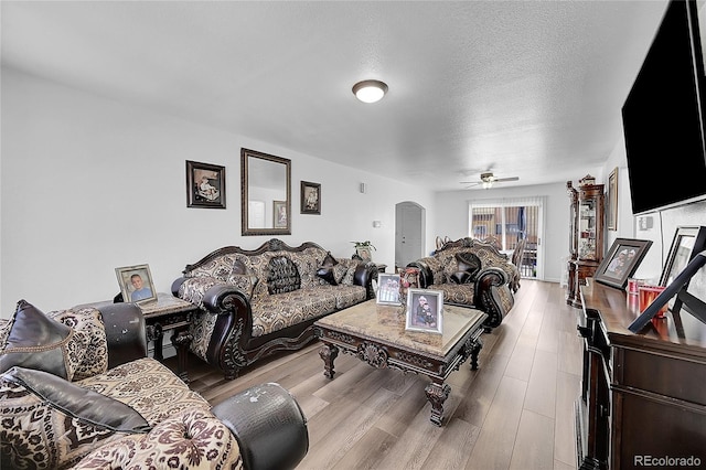 living room featuring ceiling fan, a textured ceiling, and light wood-type flooring