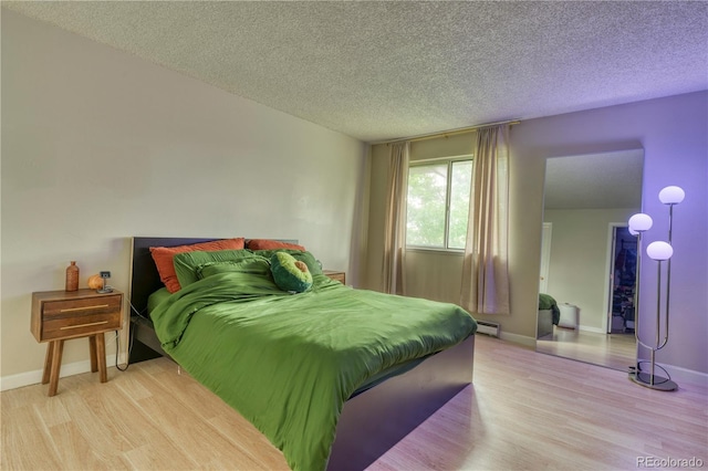 17595 E Mansfield Ave Unit 1331L, Aurora, CO 80013 - bedroom featuring light wood-style flooring, a baseboard heating unit, a textured ceiling, and baseboards
