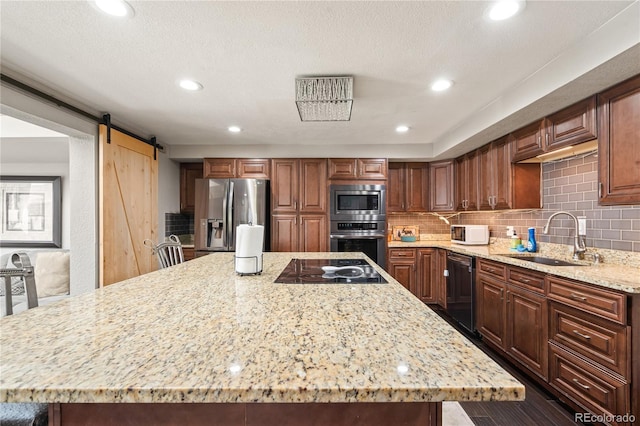 3625 Chase St, Wheat Ridge, CO 80212 - kitchen with black appliances, a sink, a spacious island, light stone countertops, and a barn door