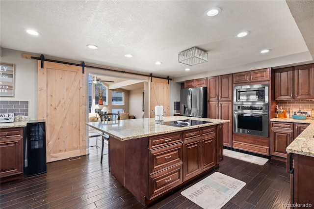 3625 Chase St, Wheat Ridge, CO 80212 - kitchen featuring a barn door, appliances with stainless steel finishes, decorative backsplash, a kitchen breakfast bar, and dark wood finished floors