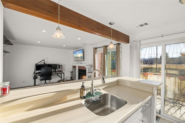 kitchen featuring beam ceiling, decorative light fixtures, visible vents, a sink, and a warm lit fireplace