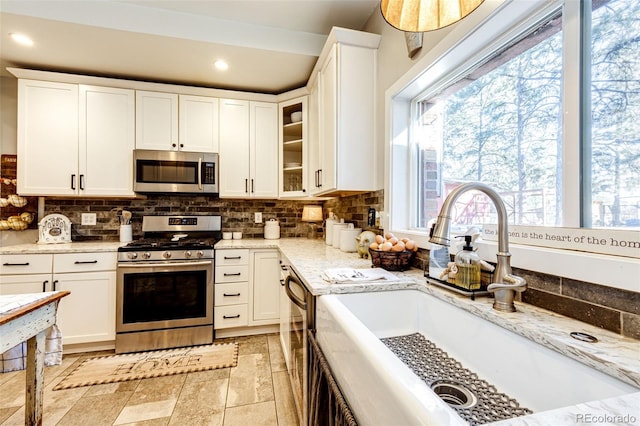 kitchen with appliances with stainless steel finishes, backsplash, a sink, and white cabinetry