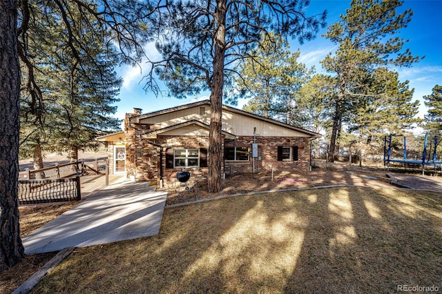 rear view of property with driveway, brick siding, a trampoline, and a chimney