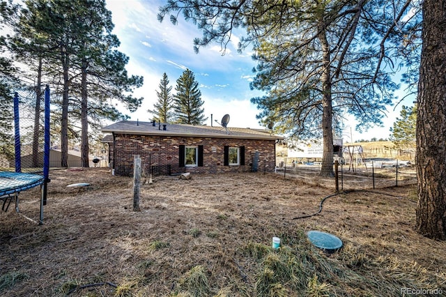 rear view of property featuring a trampoline, brick siding, and fence