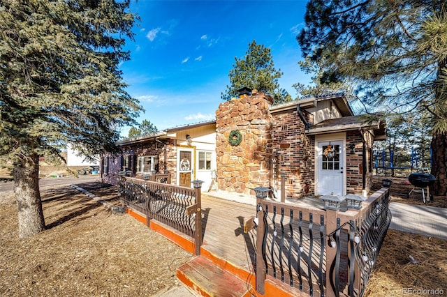 view of front of home featuring a deck, stone siding, brick siding, and a chimney