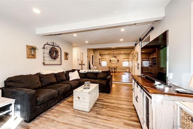 living area featuring light wood-style floors, a barn door, beamed ceiling, and recessed lighting