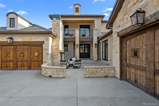 back of property with driveway, stucco siding, a balcony, and stone siding