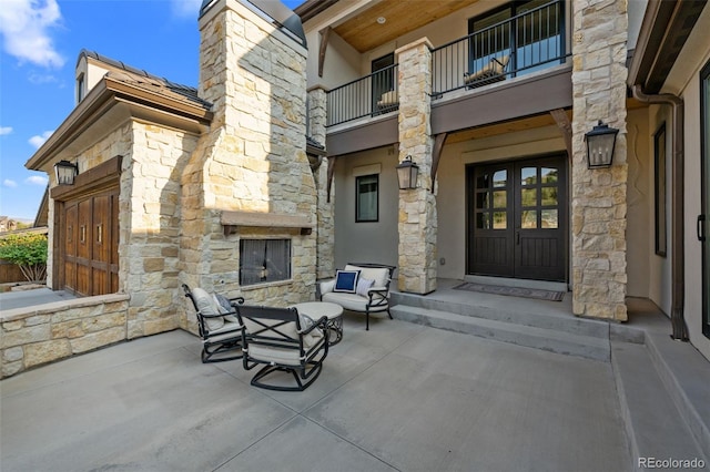 view of patio featuring french doors, an outdoor stone fireplace, and a balcony