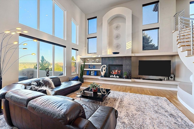 living room with a tiled fireplace, a high ceiling, and hardwood / wood-style flooring