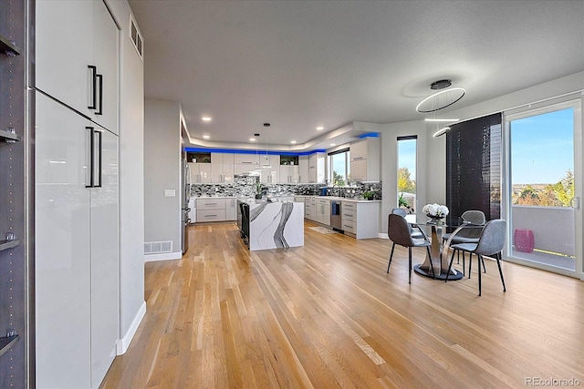 interior space featuring backsplash, extractor fan, a center island, white cabinetry, and light hardwood / wood-style flooring