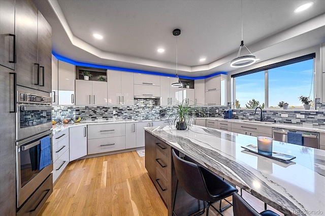 kitchen featuring decorative light fixtures, backsplash, light hardwood / wood-style floors, a raised ceiling, and white cabinetry