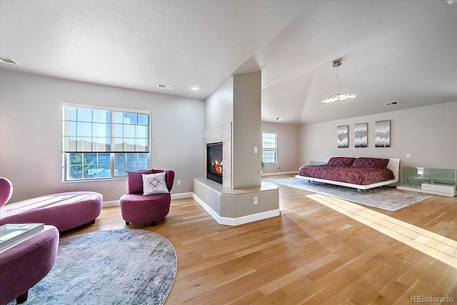 bedroom featuring wood-type flooring, vaulted ceiling, a textured ceiling, and a fireplace