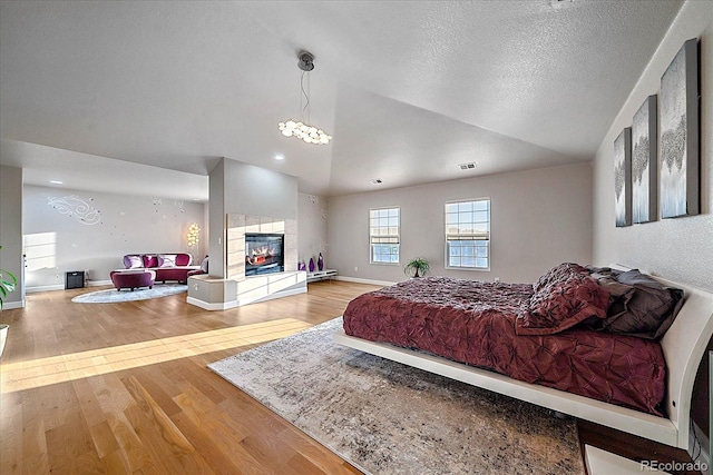 bedroom featuring a tiled fireplace, vaulted ceiling, and hardwood / wood-style flooring