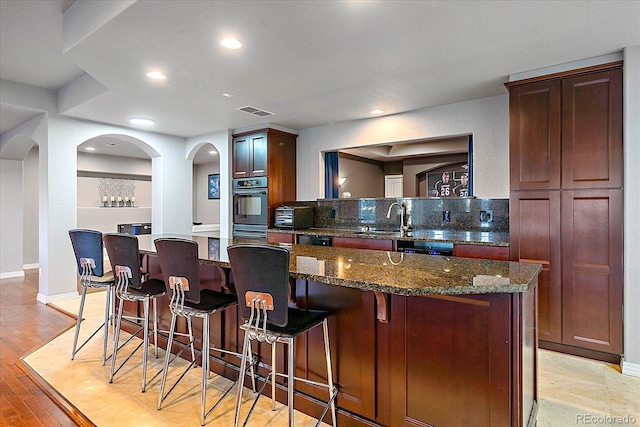 kitchen with dishwasher, a center island, dark stone counters, light hardwood / wood-style floors, and sink