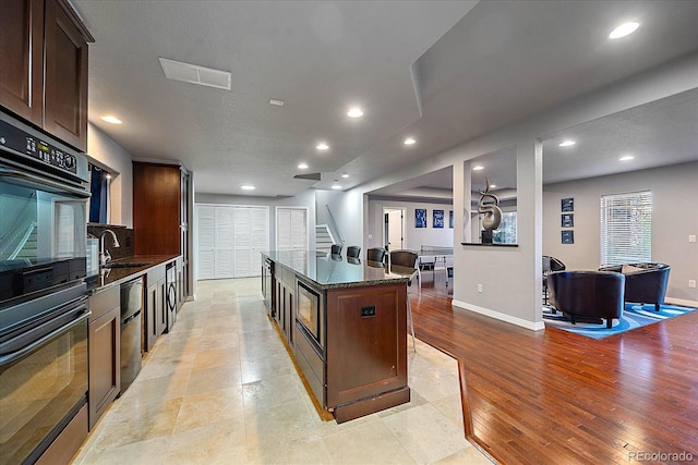 kitchen featuring a center island, sink, black double oven, dark brown cabinetry, and dark stone counters