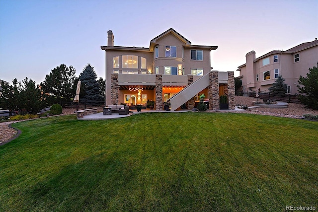 back house at dusk with a wooden deck, a lawn, and a patio