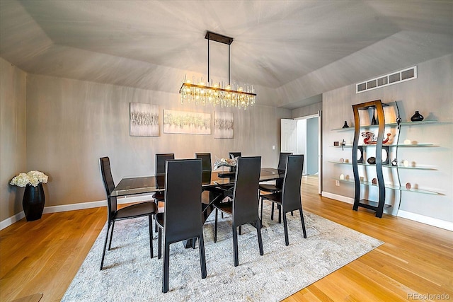 dining space with hardwood / wood-style floors, lofted ceiling, and an inviting chandelier