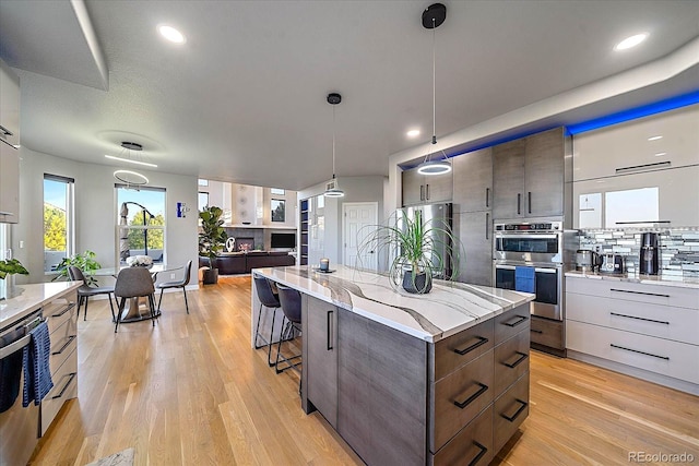 kitchen featuring light hardwood / wood-style floors, stainless steel appliances, tasteful backsplash, pendant lighting, and a center island