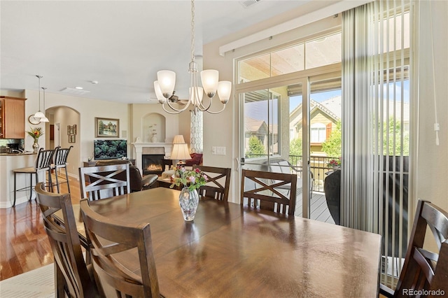 10064 Bluffmont Ct, Lone Tree, CO 80124 - dining space with arched walkways, a glass covered fireplace, a chandelier, and wood finished floors