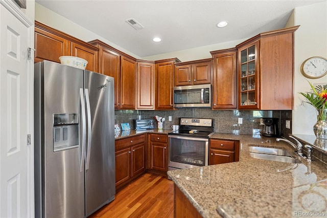 10064 Bluffmont Ct, Lone Tree, CO 80124 - kitchen featuring appliances with stainless steel finishes, wood finished floors, light stone counters, glass insert cabinets, and recessed lighting