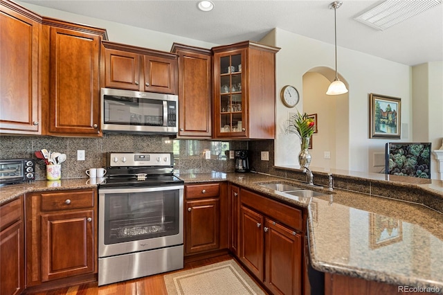 10064 Bluffmont Ct, Lone Tree, CO 80124 - kitchen featuring appliances with stainless steel finishes, arched walkways, glass insert cabinets, dark stone counters, and recessed lighting