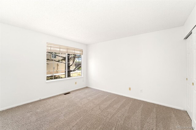 carpeted empty room featuring baseboards, a textured ceiling, and visible vents