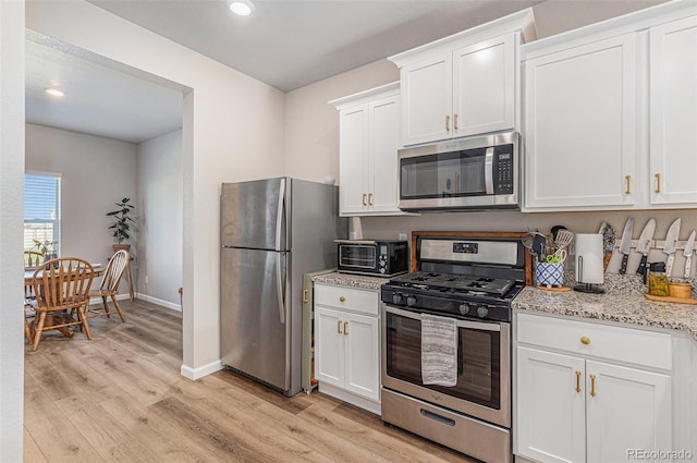 kitchen with light stone countertops, light hardwood / wood-style floors, white cabinets, and appliances with stainless steel finishes