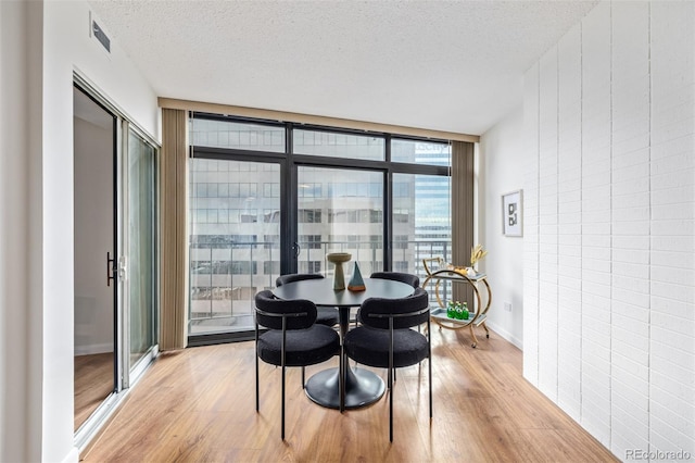 dining space with a wall of windows, light hardwood / wood-style floors, and a textured ceiling