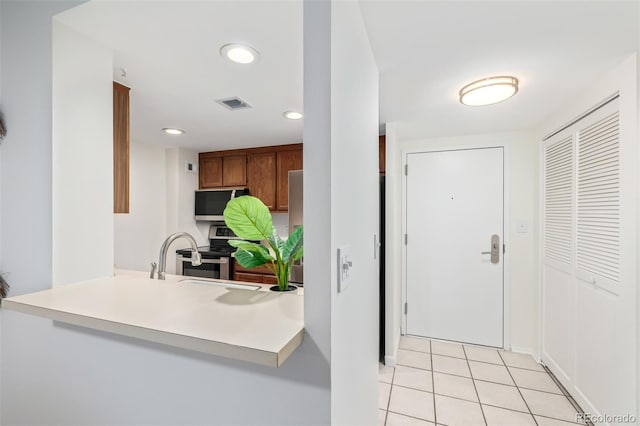 kitchen featuring sink, kitchen peninsula, light tile patterned floors, and stainless steel electric range