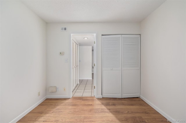 unfurnished bedroom with a closet, a textured ceiling, and light wood-type flooring