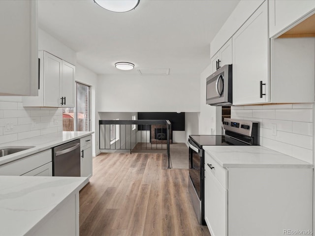 kitchen featuring white cabinets, light wood-style flooring, appliances with stainless steel finishes, light stone counters, and backsplash