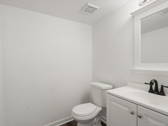 half bathroom with toilet, wood finished floors, vanity, visible vents, and baseboards