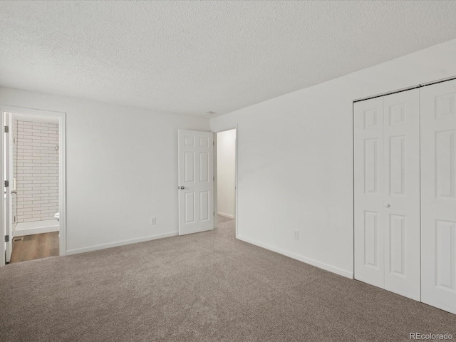 unfurnished bedroom featuring baseboards, ensuite bathroom, a textured ceiling, carpet floors, and a closet