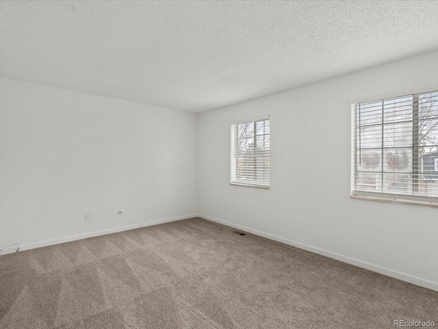 empty room featuring a textured ceiling, carpet, visible vents, and baseboards