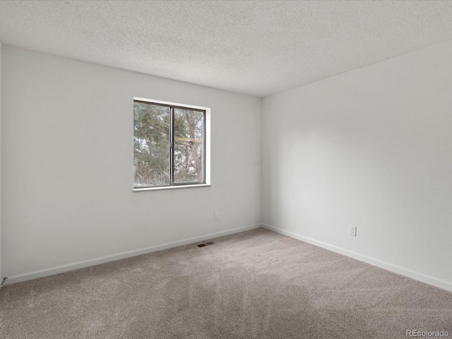 spare room featuring carpet floors, visible vents, a textured ceiling, and baseboards