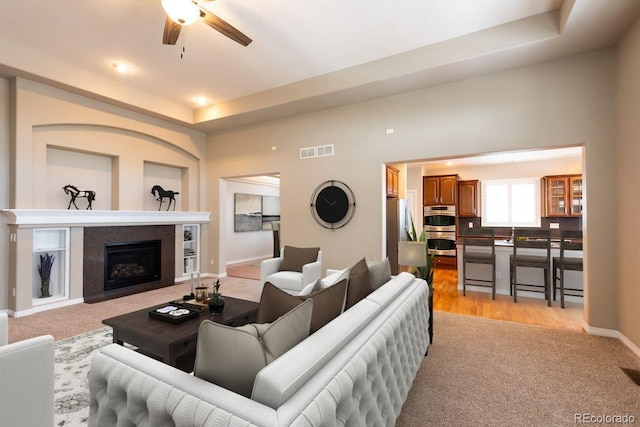 carpeted living room featuring a raised ceiling and ceiling fan