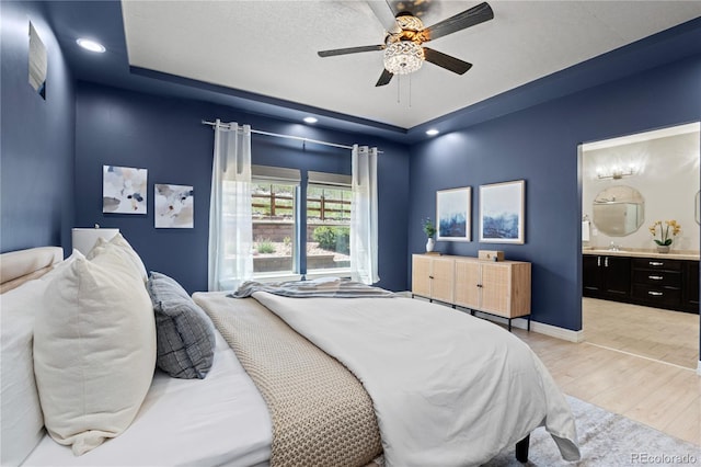 1815 Avery Way, Castle Rock, CO 80109 - bedroom featuring a tray ceiling, light wood-style floors, connected bathroom, a ceiling fan, and recessed lighting