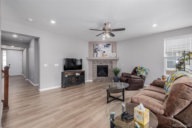 living room with a tiled fireplace, ceiling fan, and light hardwood / wood-style flooring