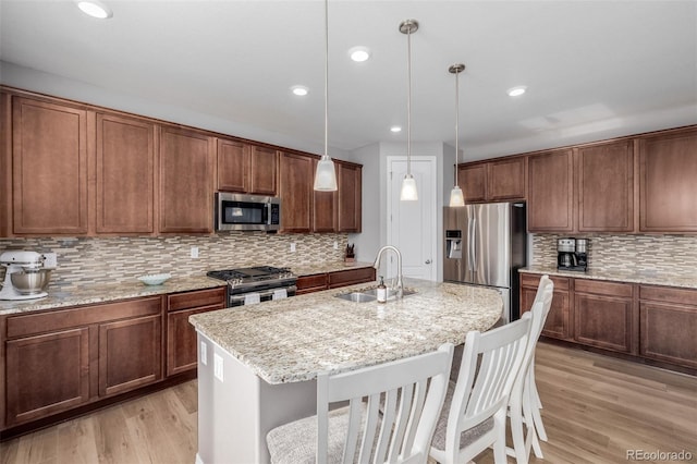 kitchen featuring stainless steel appliances, sink, pendant lighting, a center island with sink, and light hardwood / wood-style flooring