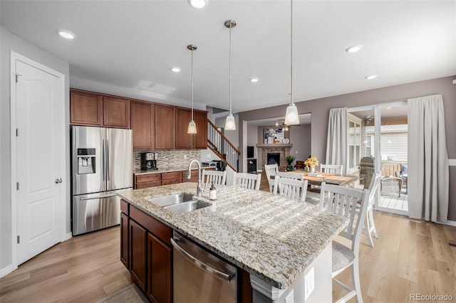 kitchen featuring a kitchen island with sink, sink, hanging light fixtures, a fireplace, and stainless steel appliances