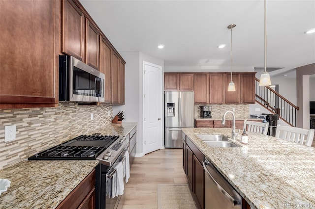 kitchen featuring pendant lighting, sink, light hardwood / wood-style flooring, light stone countertops, and stainless steel appliances