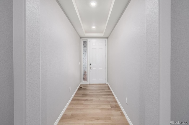 corridor with a raised ceiling and light hardwood / wood-style flooring