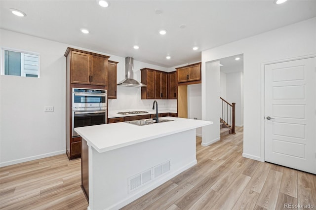 2102 Wagon Wheel Aly, Brighton, CO 80601 - kitchen featuring wall chimney range hood, appliances with stainless steel finishes, light wood-type flooring, light countertops, and an island with sink